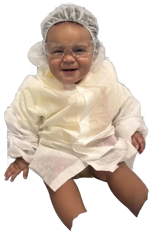 A laughing baby dressed as a little scientist, in a paper gown, cap and safety goggles.