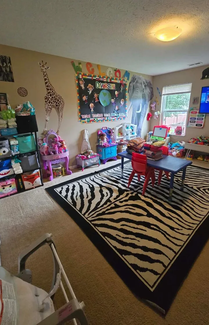 The playroom: a zebra-print rug, a small blue table with red chairs, shelves of toys, and a Welcome board on the wall.